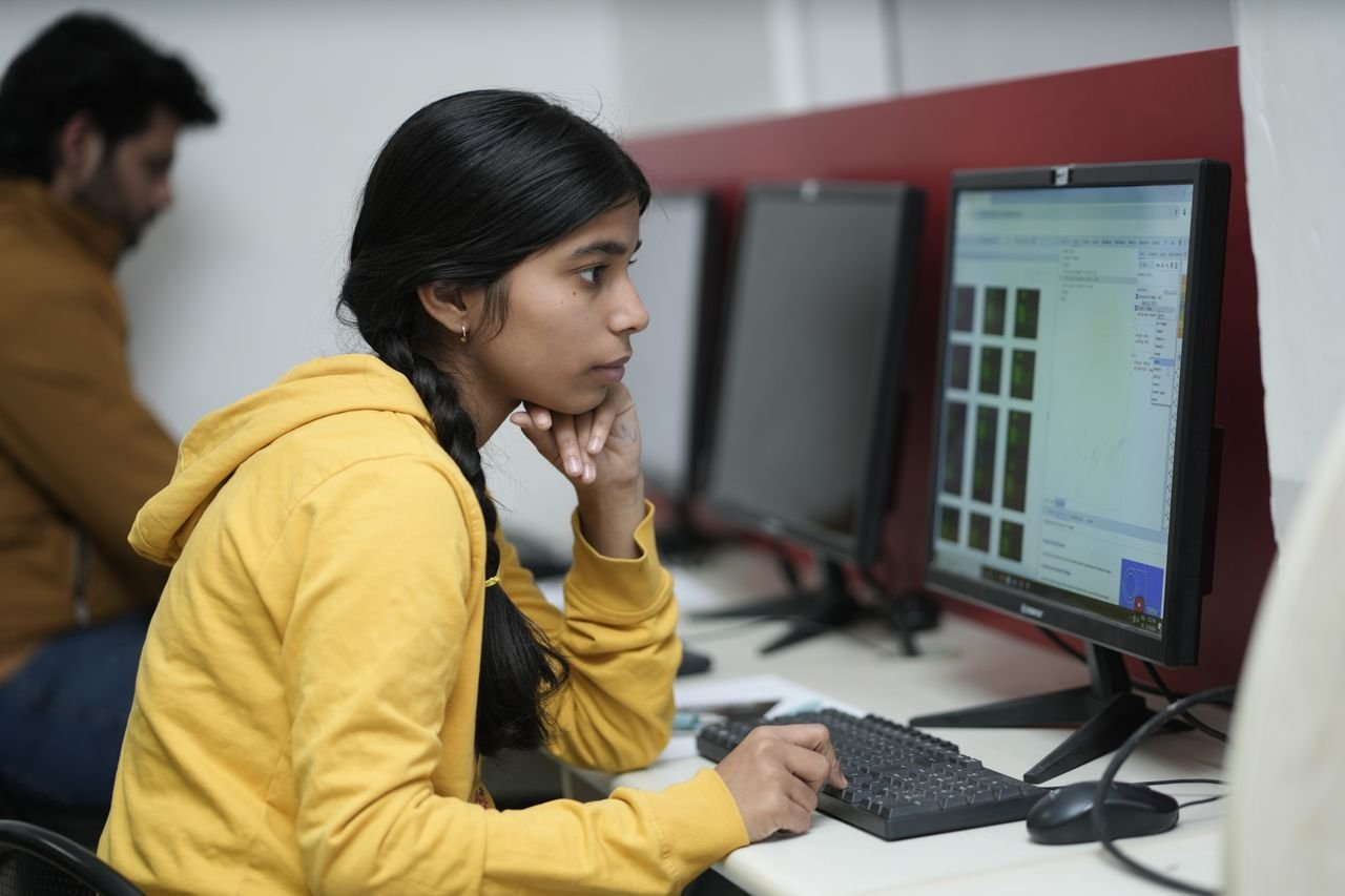 Woman in yellow hoodie focused on computer work, indoor office.