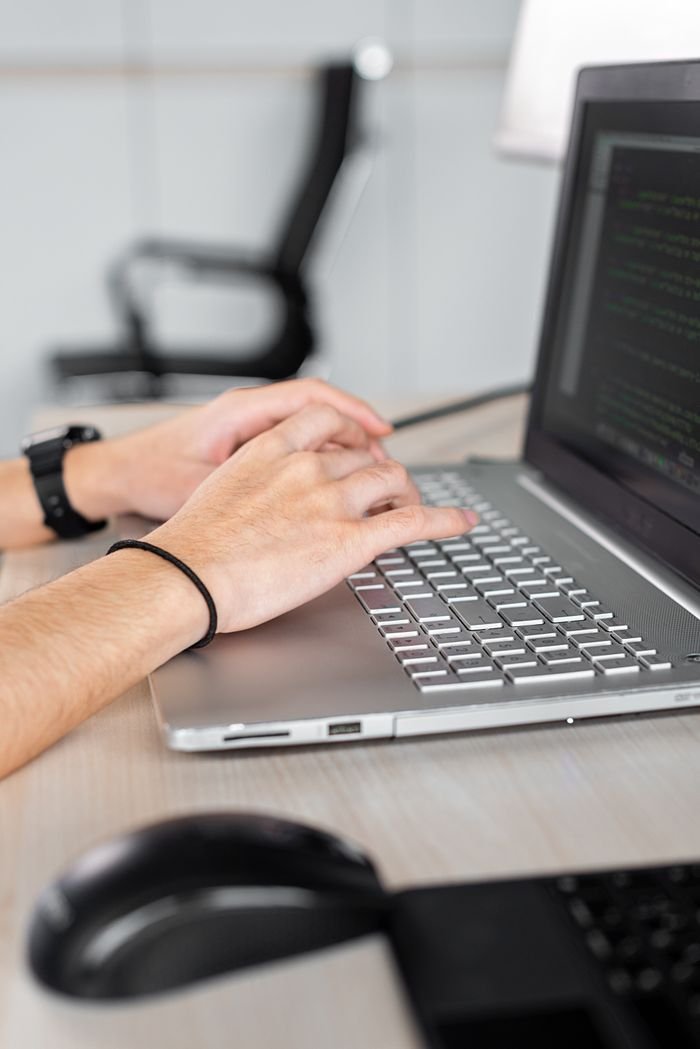 Person typing on a laptop, focusing on hands and code on screen in a modern office.